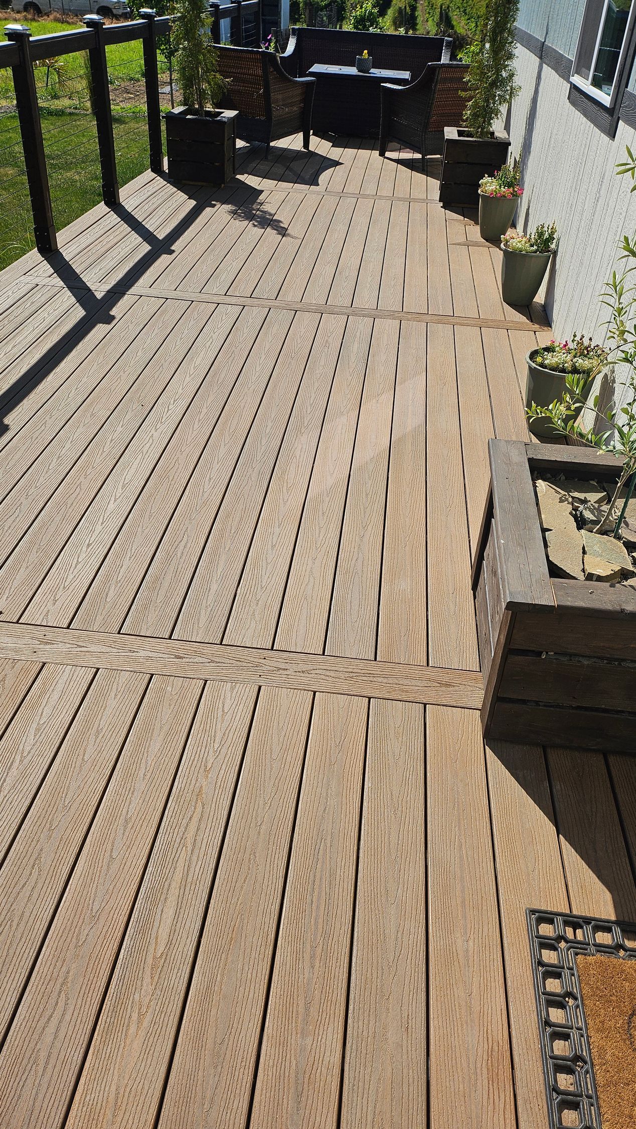 A newly installed gray composite deck with two steps leading down to a patch of dirt and grass in a backyard.