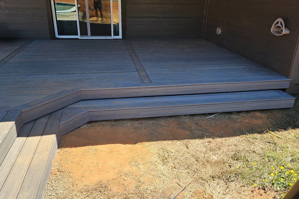A low-level deck with gray composite boards and two wide steps leading down to a patch of dirt and sparse grass.