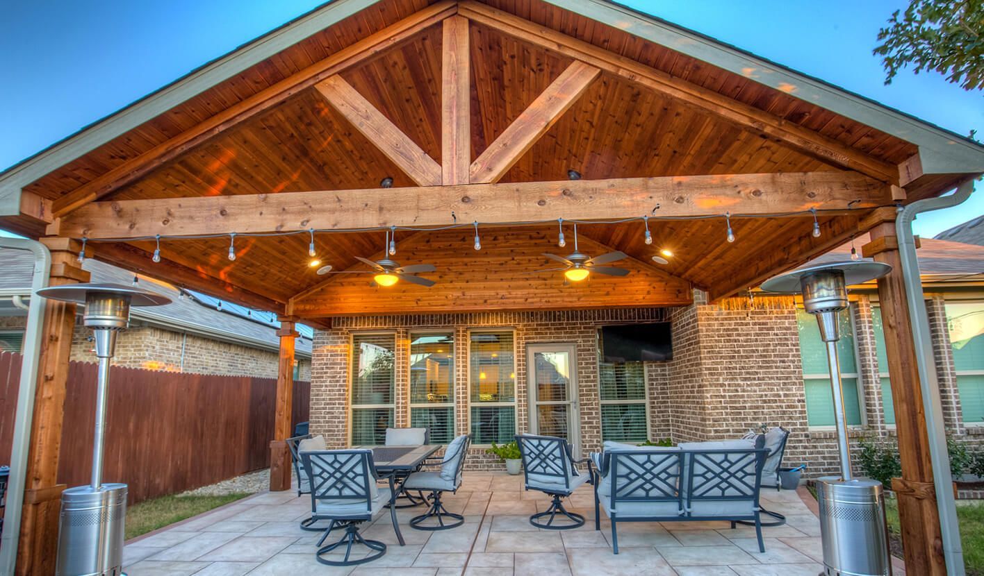 A stone-paved patio faces a building wall made of a rustic stone base, wooden framing, and long, dark-wood lattice windows.