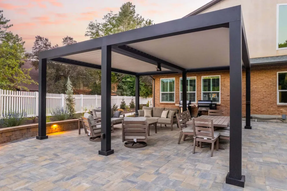 A long wooden deck walkway features round pillars, slatted walls, and a warm, sunlit view of a lush green garden.