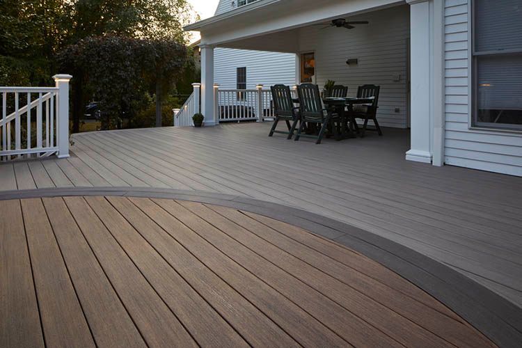 Two people work on a newly constructed wooden deck attached to a house on a sunny day.