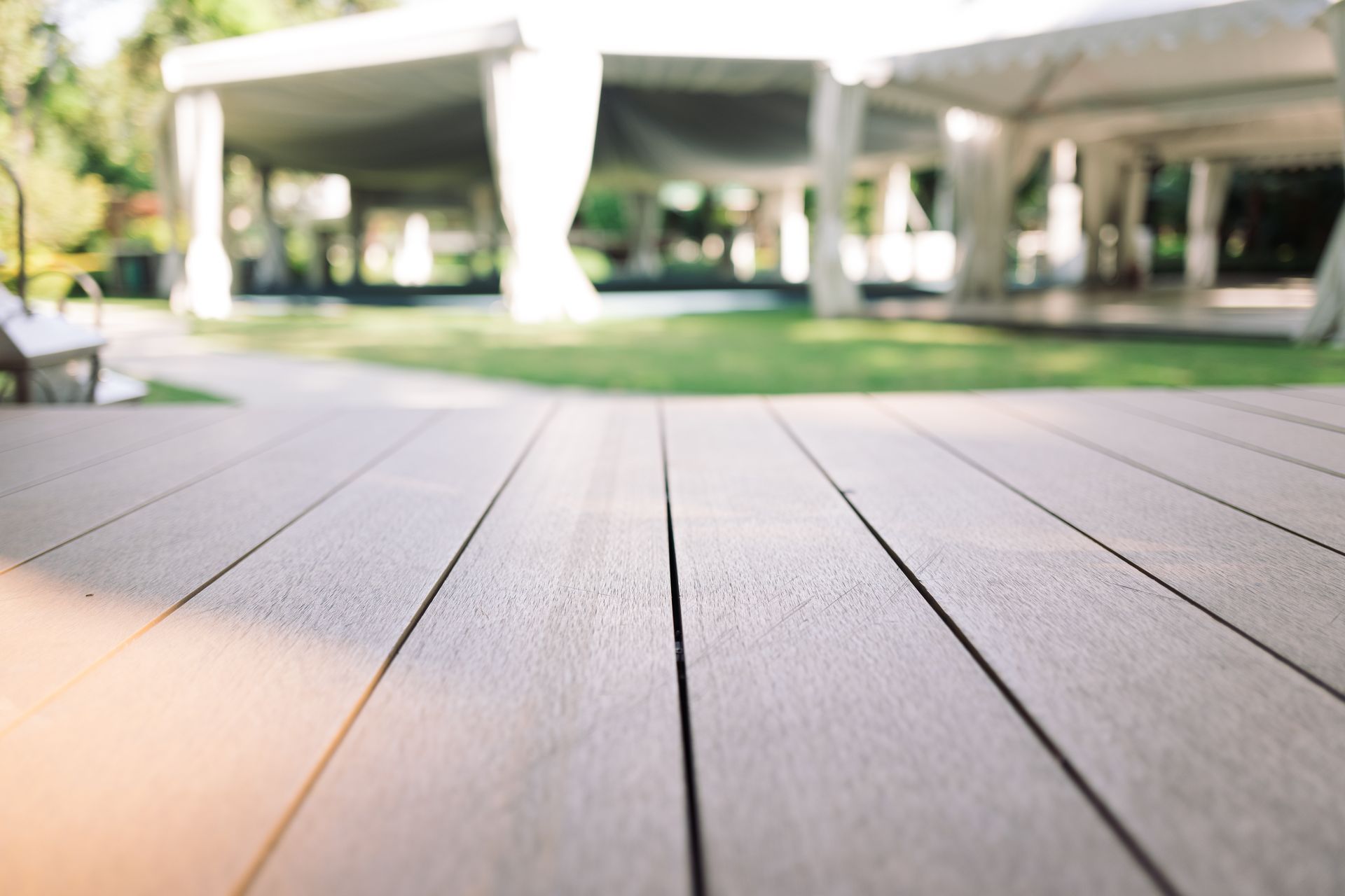 Wooden deck leading to a blurred outdoor pavilion with concrete pillars and green lawn