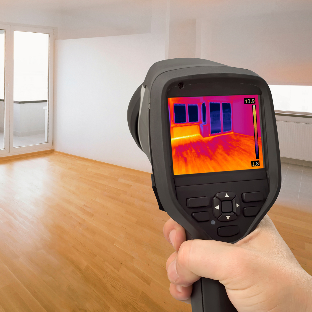 A person is holding a thermal camera in front of an empty room