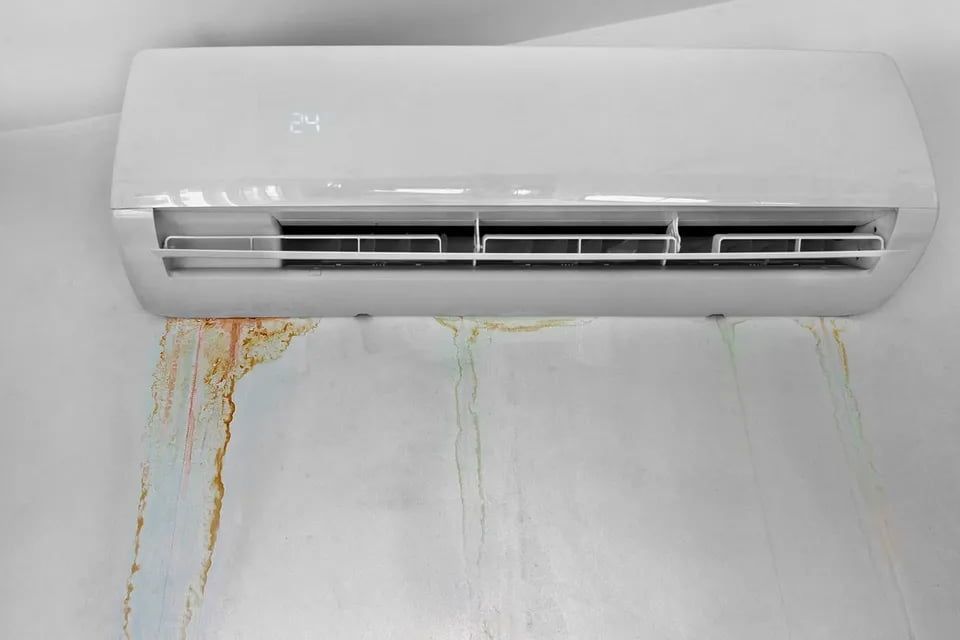 A white air conditioner is hanging on a white wall with water damage.