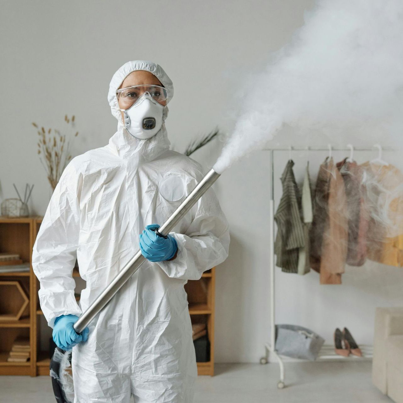 A man in a protective suit is spraying a room with a sprayer.