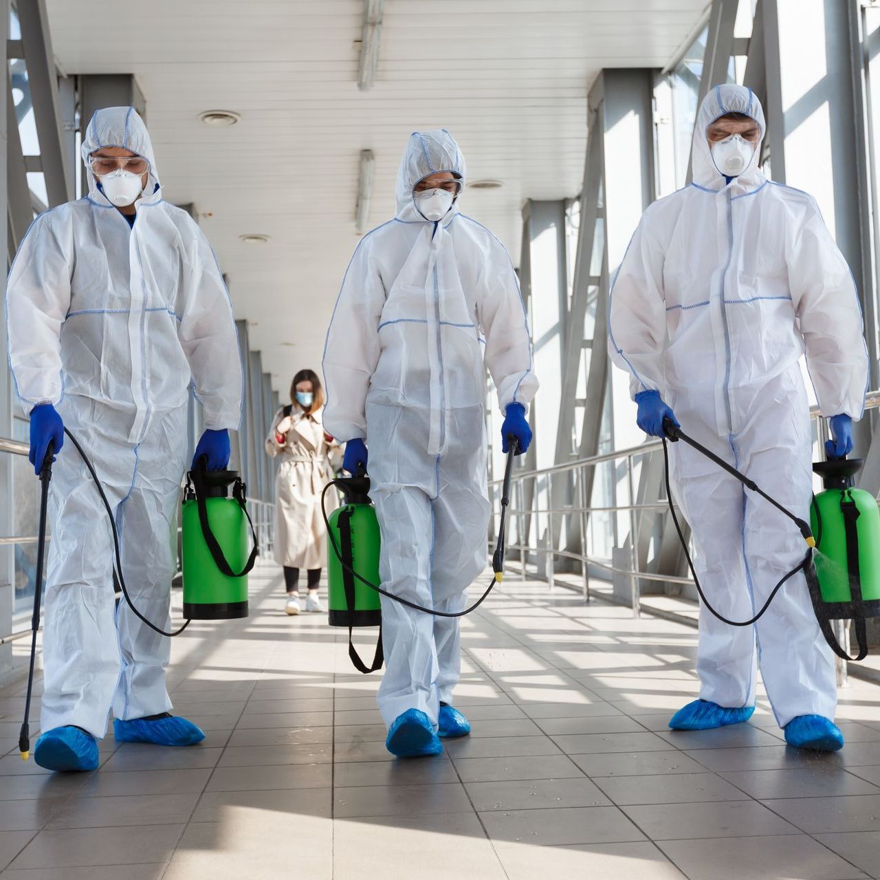 A group of people wearing protective suits and masks are spraying chemicals on a walkway.