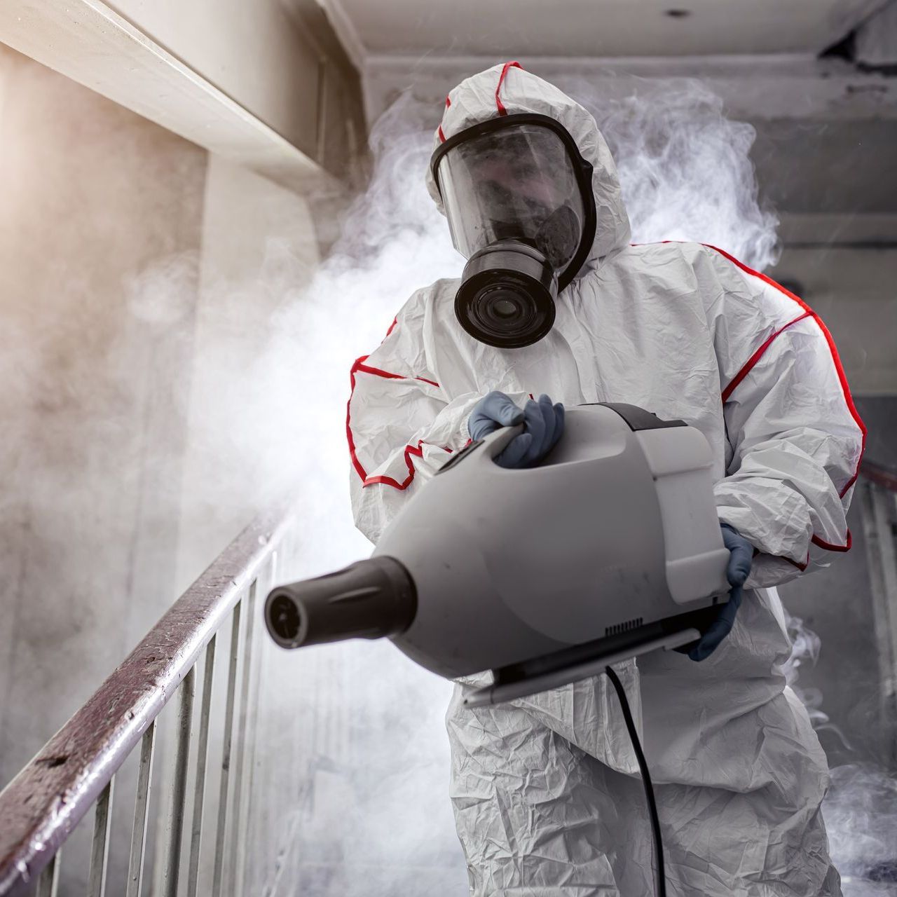 A man in a protective suit and gas mask is holding a sprayer.