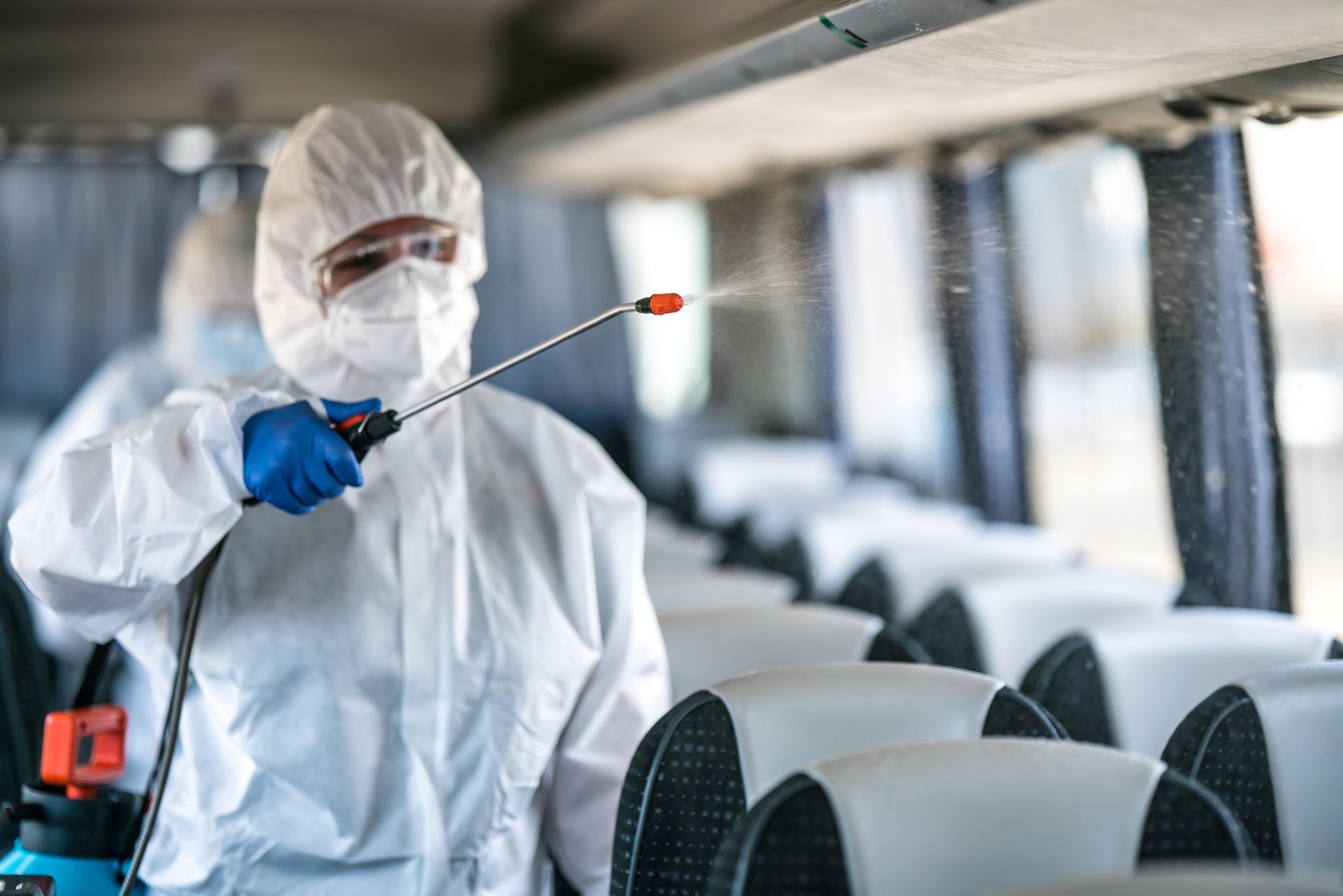 A man in a protective suit is spraying a bus with a sprayer.