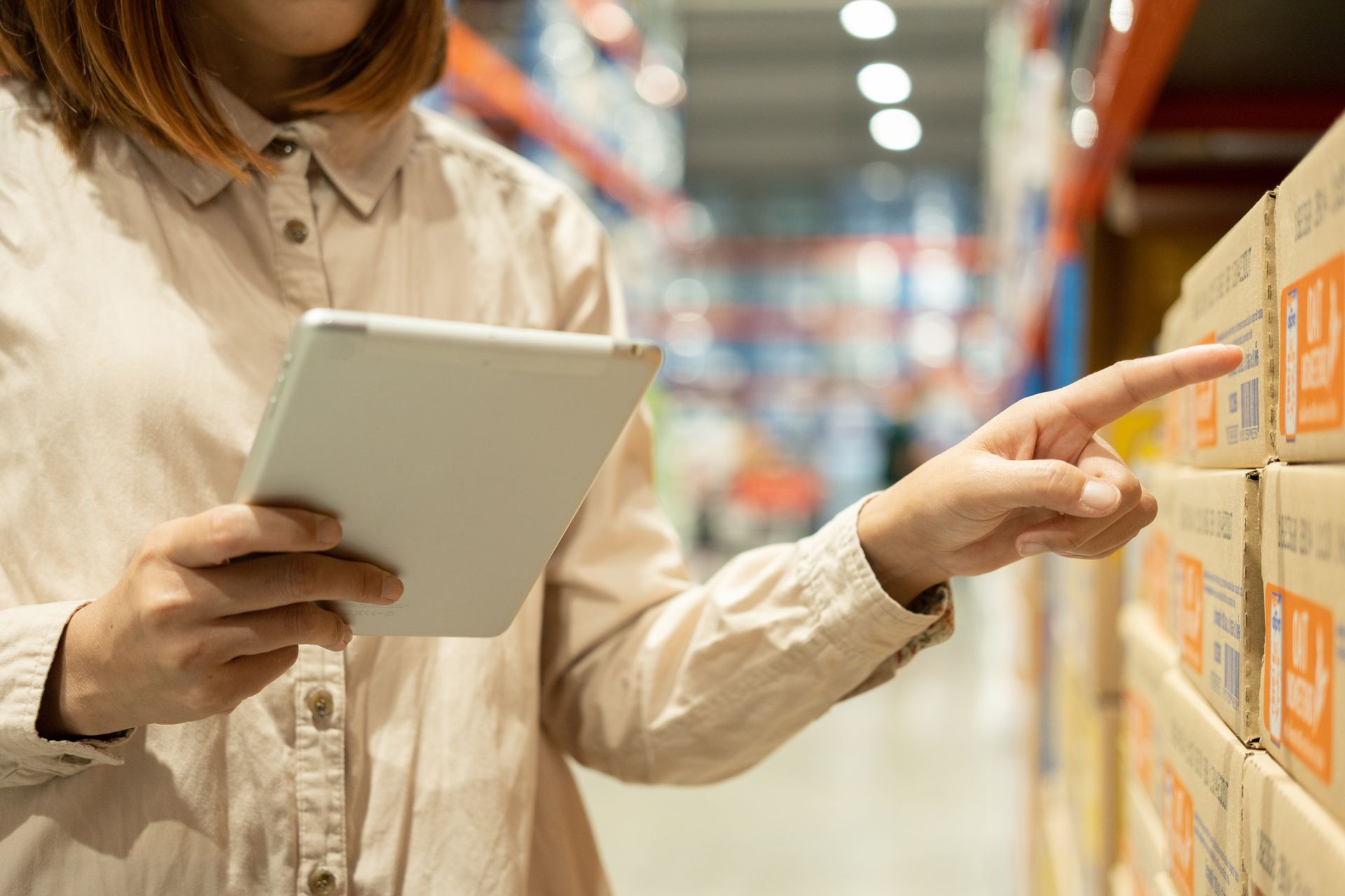 A woman is using a tablet in a warehouse and pointing at boxes.