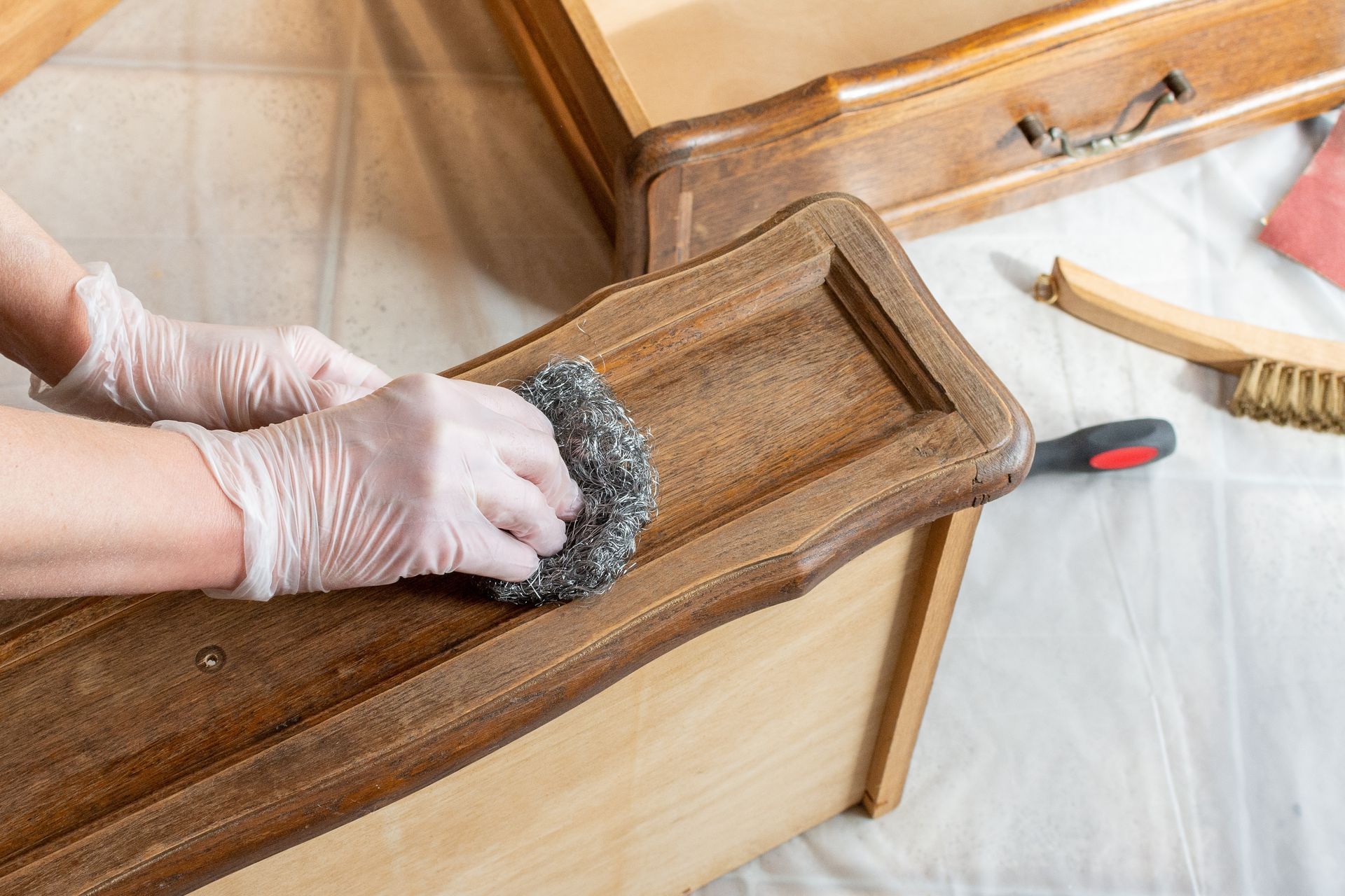 A person is cleaning a wooden drawer with a sponge.
