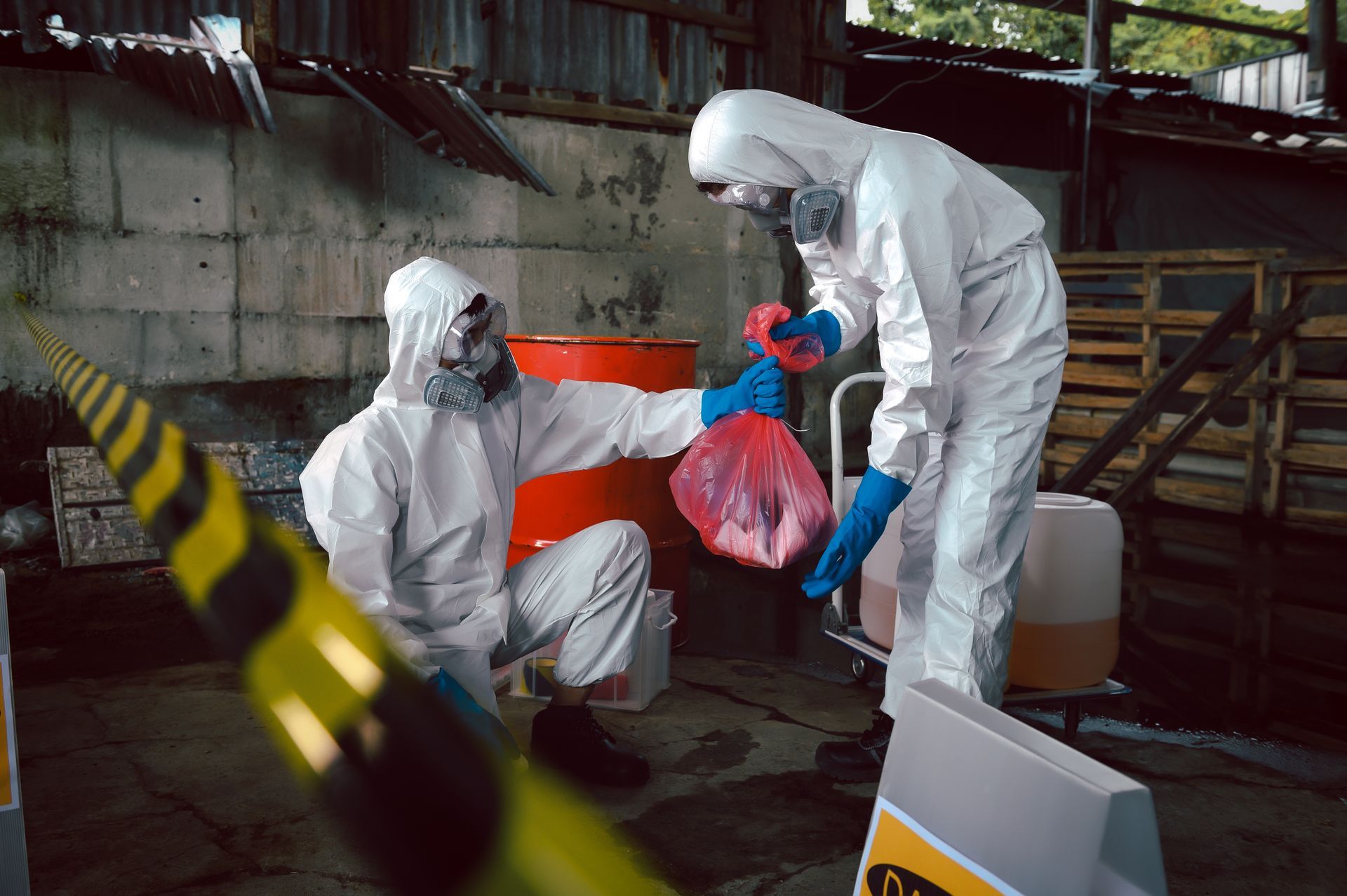 Two men in protective suits are standing next to each other cleaning biohazard material.