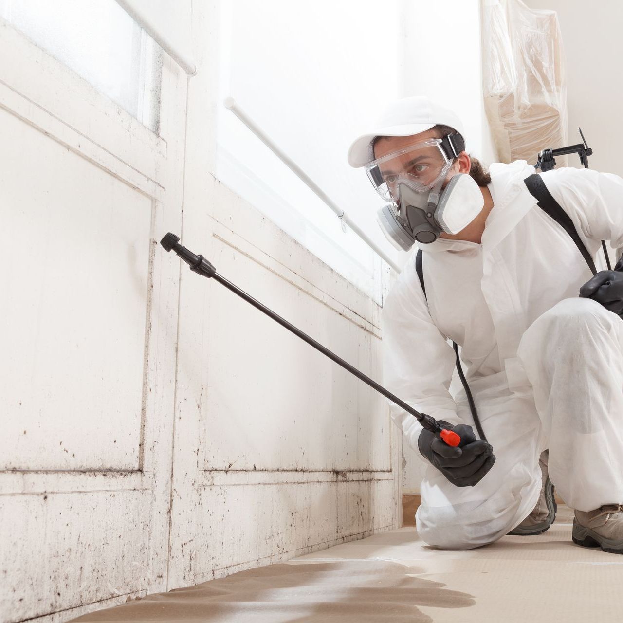 A man wearing a gas mask is spraying a wall with a sprayer.