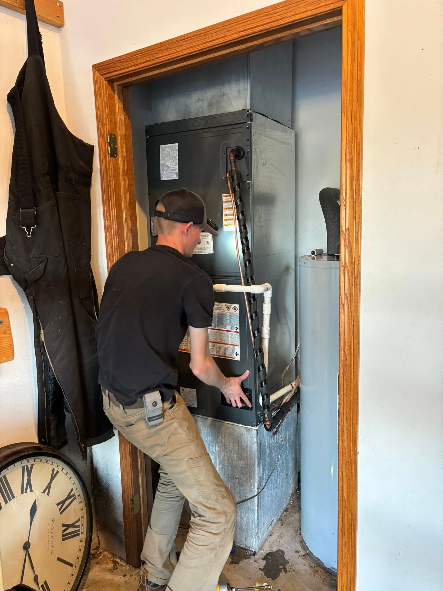 Man installing HVAC unit in a small space. He wears a black shirt and tan pants.