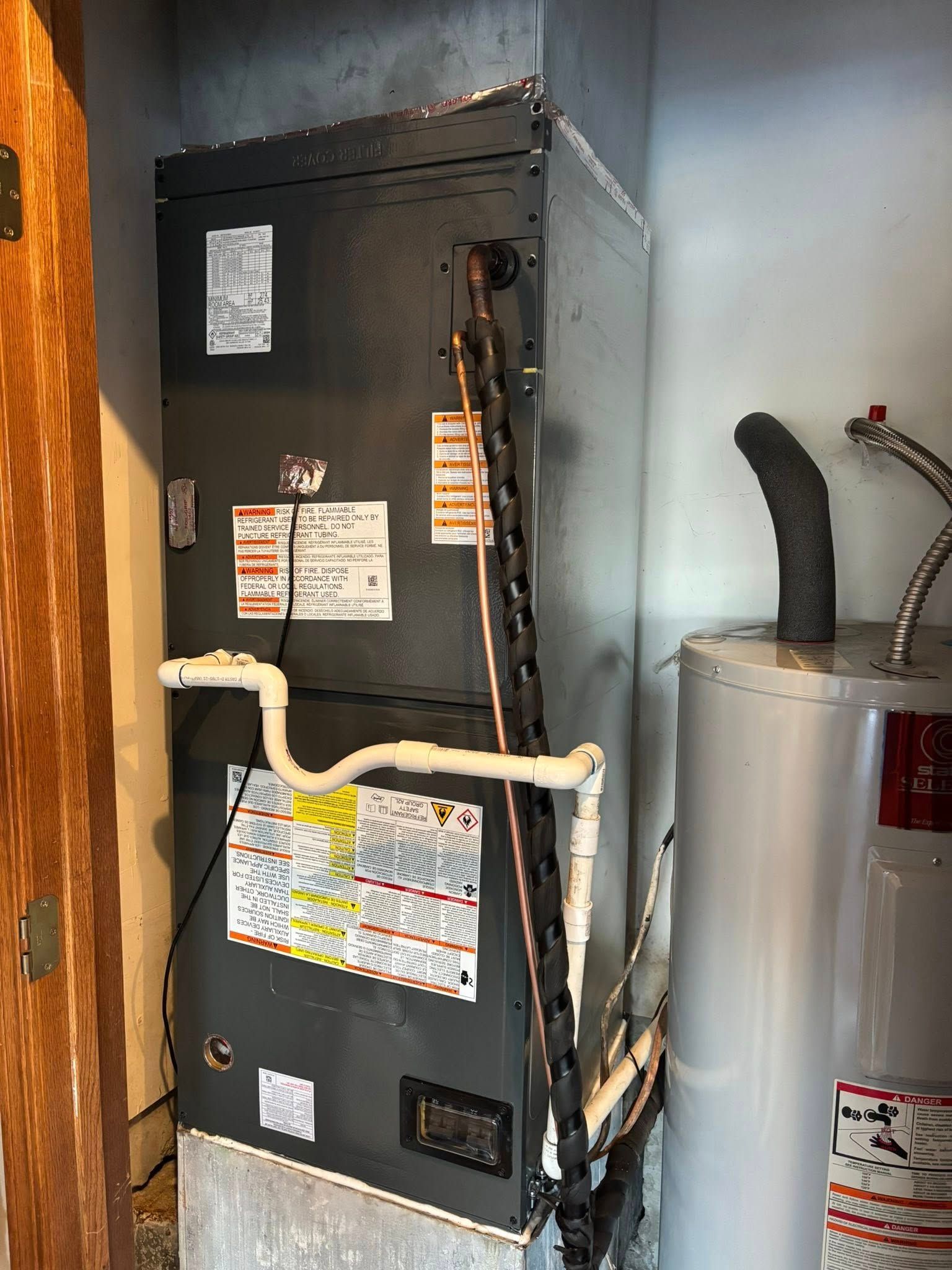 Furnace and water heater in a utility room. Gray appliances. Copper and white pipes.