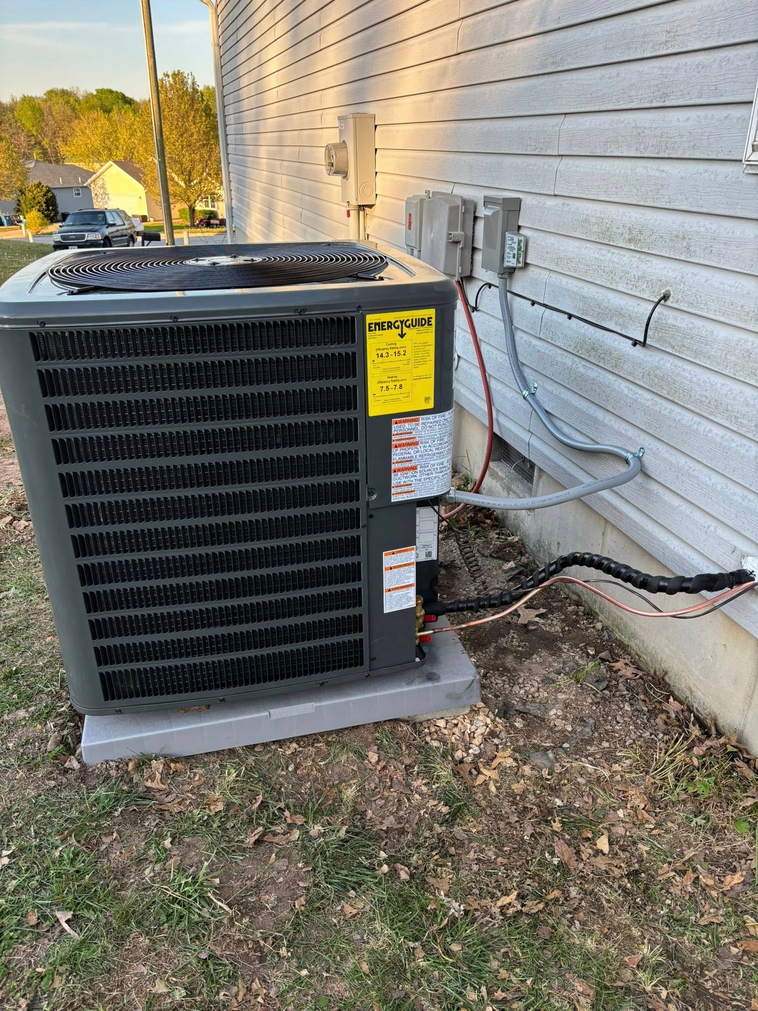 Air conditioning unit against a house, electrical wiring visible.
