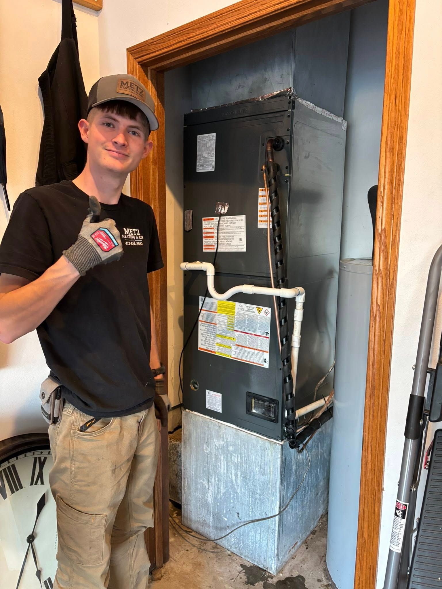 HVAC technician with thumbs up next to a large heating/cooling unit in a doorway.