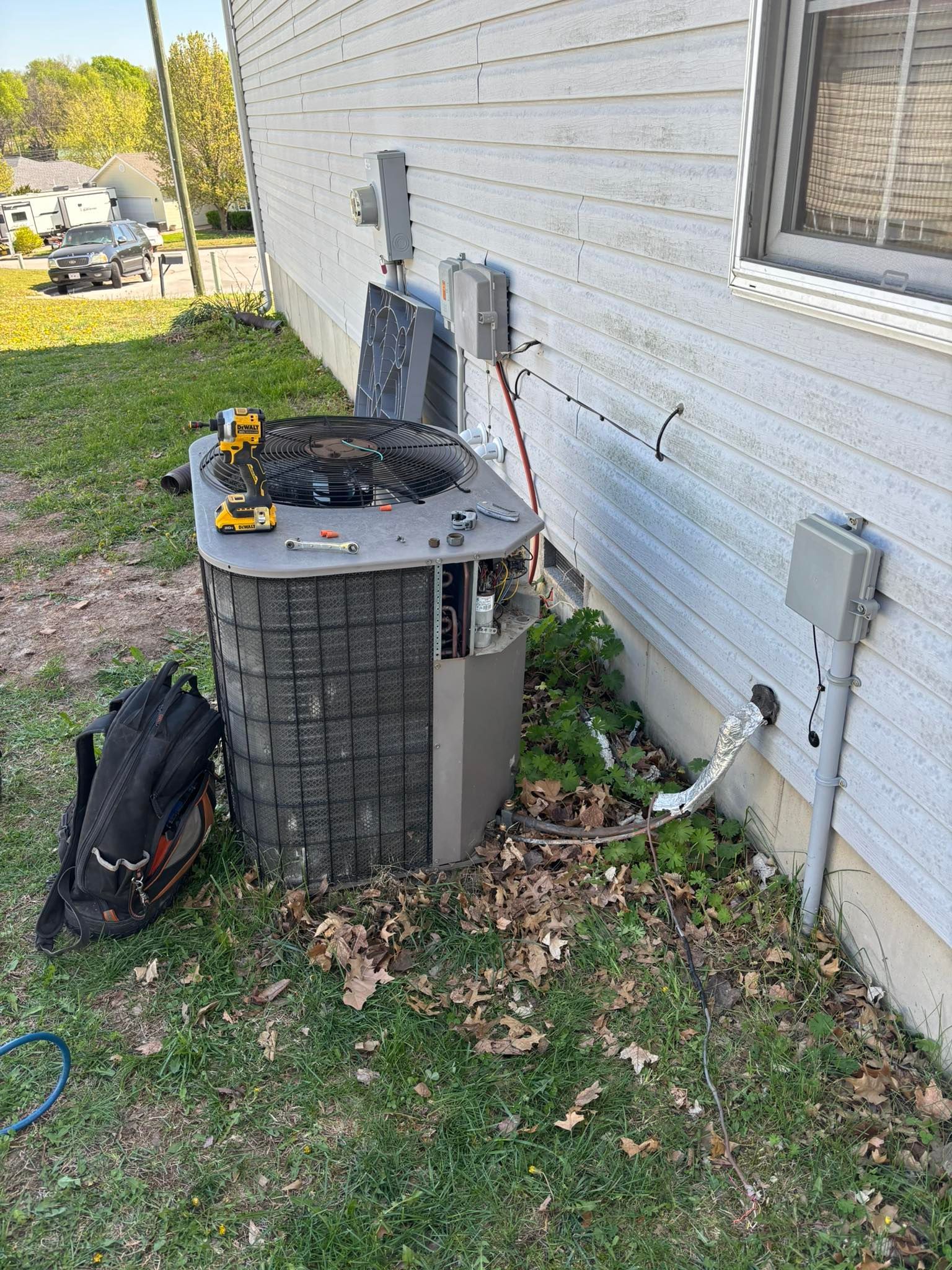AC unit being serviced outdoors; tools and backpack nearby.