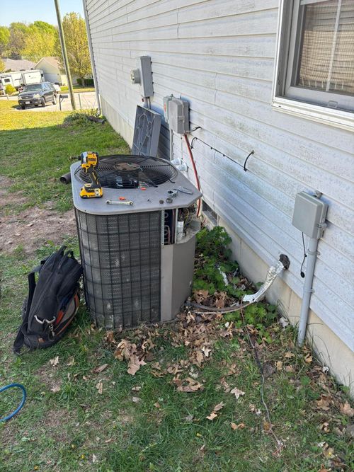 HVAC unit being serviced outdoors, tools on top. Black backpack on the ground.