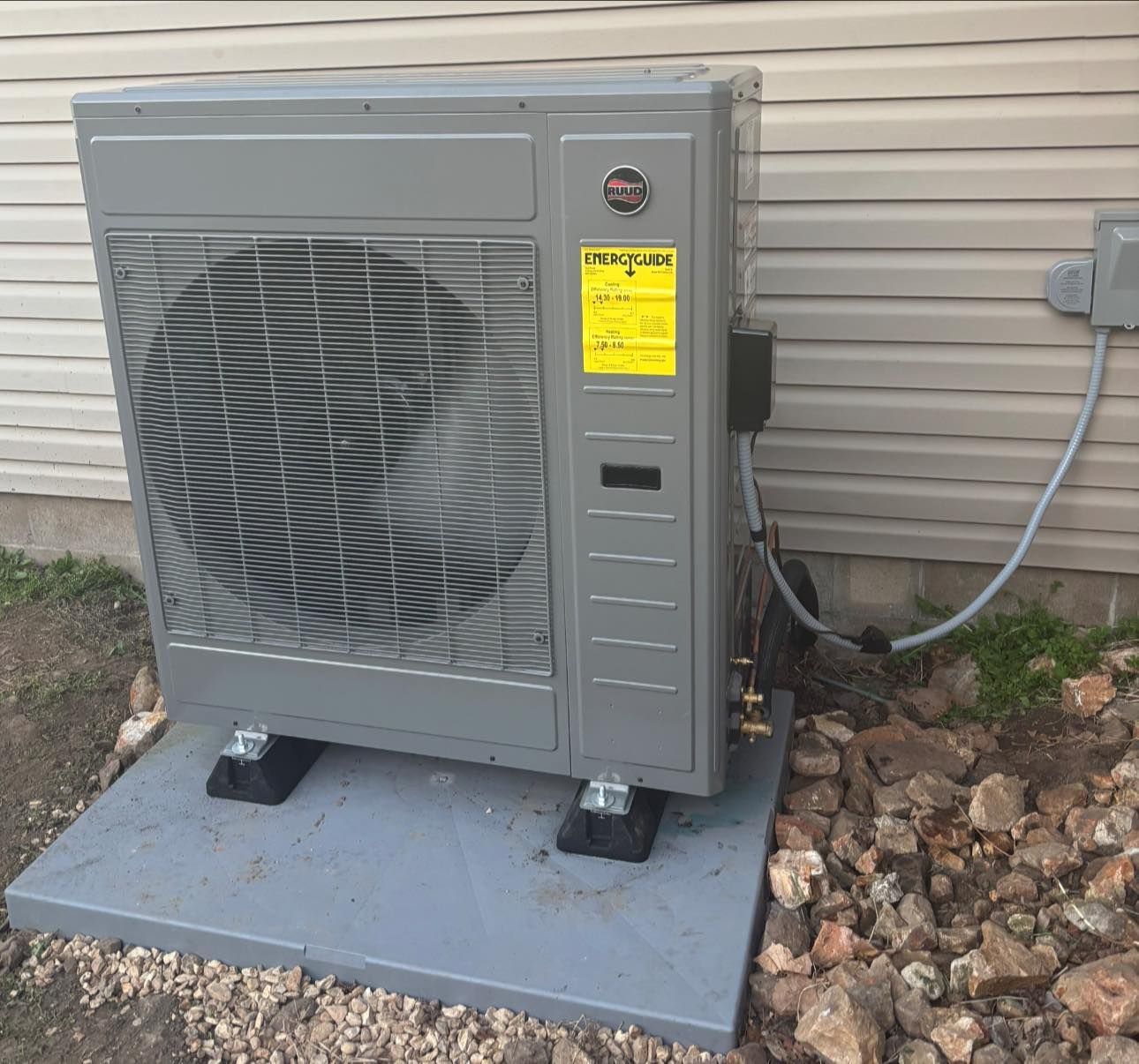 Gray air conditioning unit on a concrete pad next to a light-colored building wall.