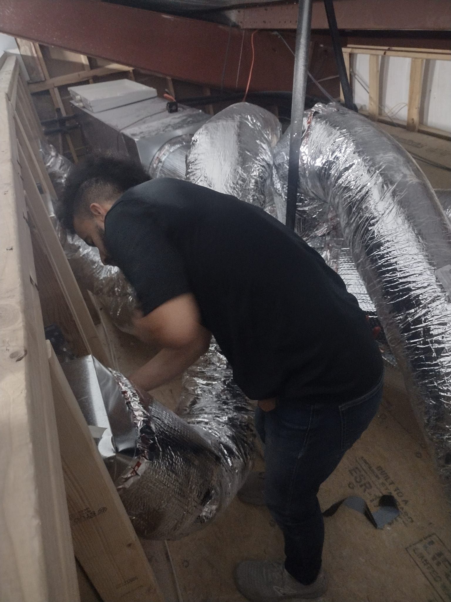 A person working with silver insulated ductwork in an attic-like space.