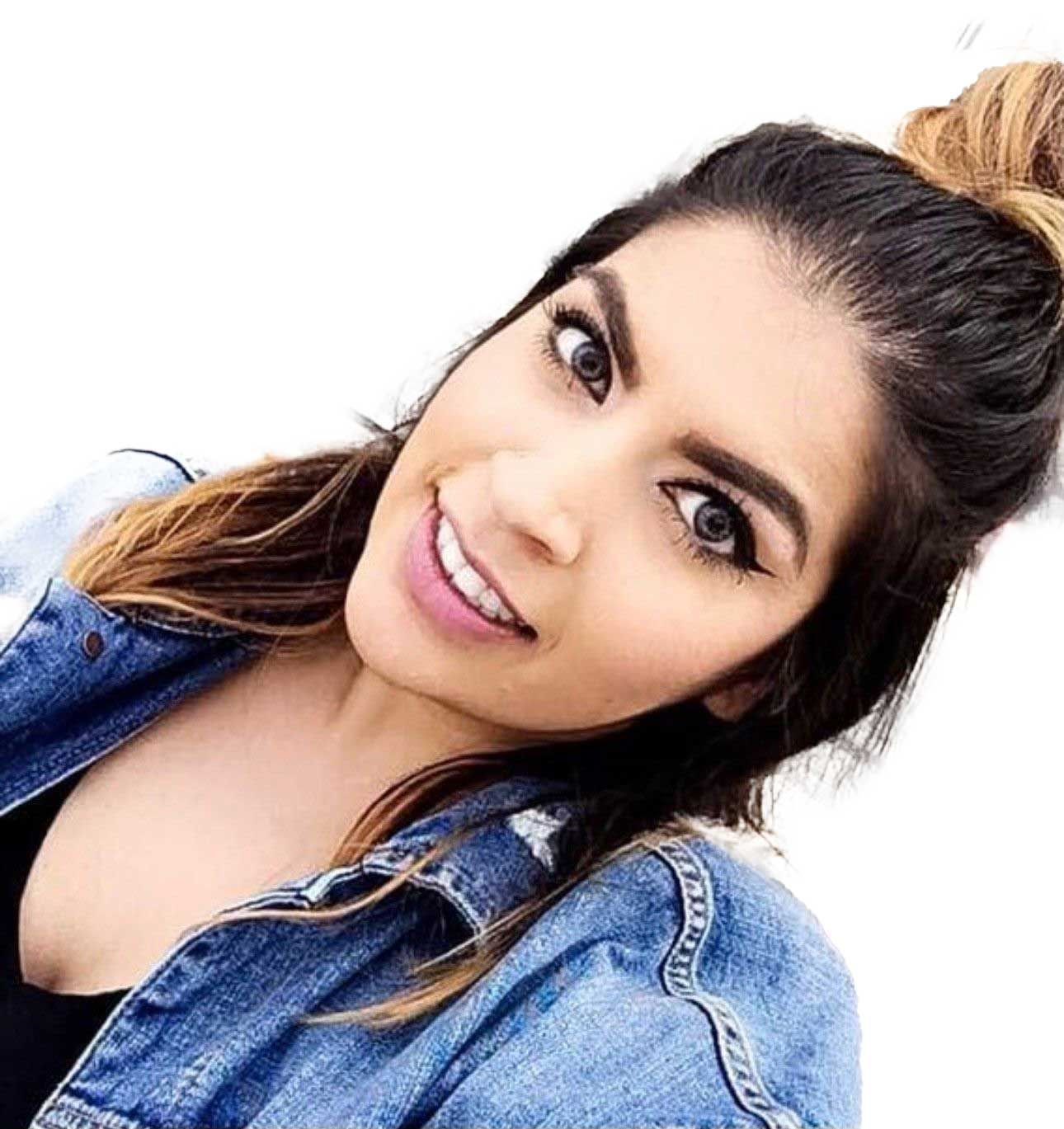 A person with long dark hair styled in a high bun, wearing a denim jacket, looking at the camera with a subtle smile.