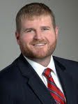 A man with a beard is wearing a suit and tie and smiling.