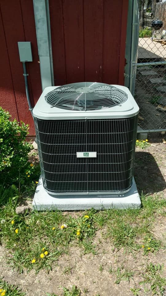 A large air conditioner is sitting in the grass in front of a red shed.
