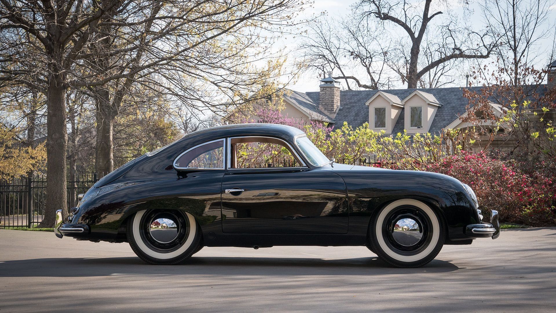 A black porsche is parked on the side of the road in front of a house.