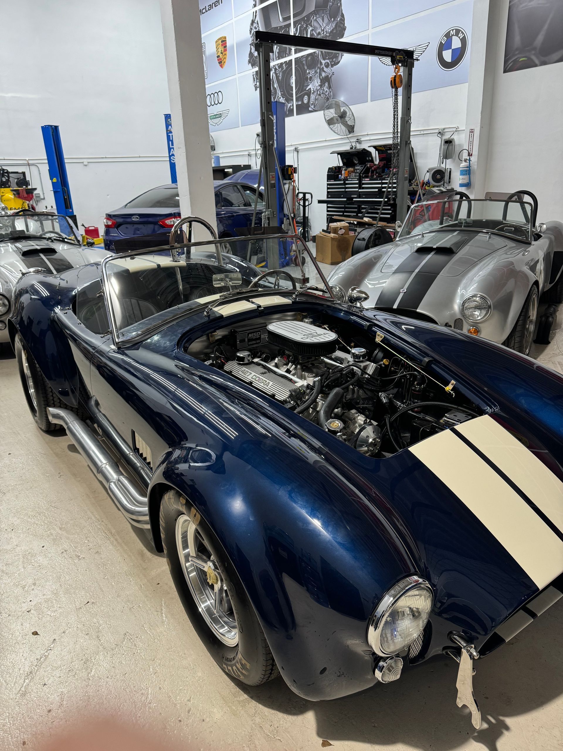 A blue sports car with the hood open is parked in a garage.