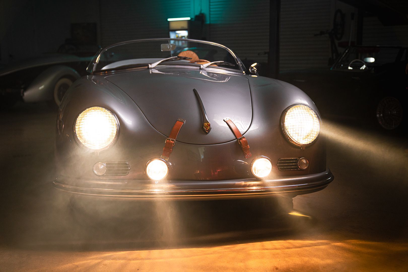 A silver porsche speedster is parked in a garage at night.