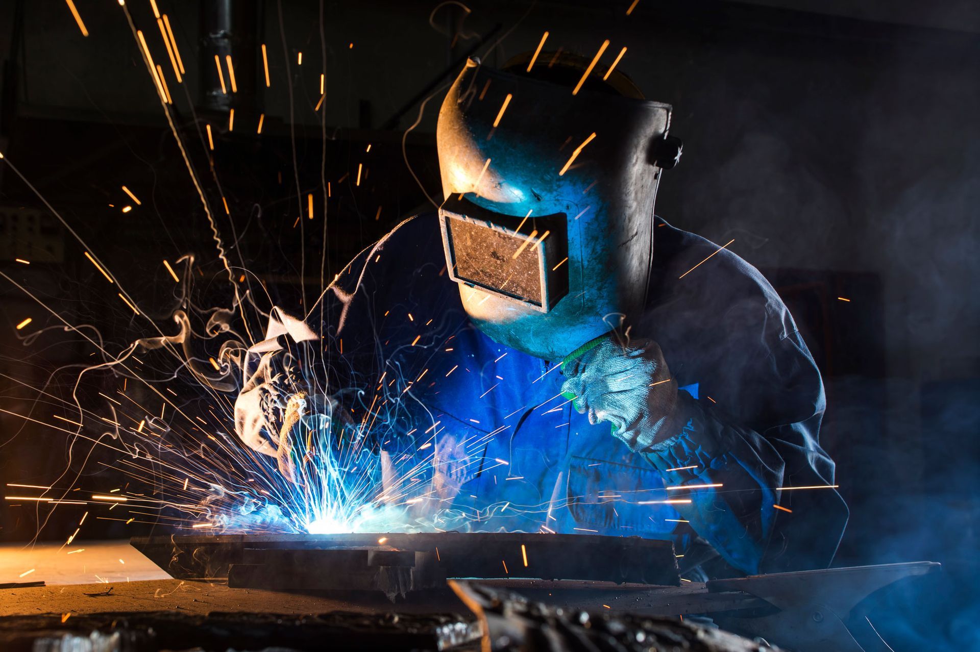 A man wearing a welding helmet is welding a piece of metal.