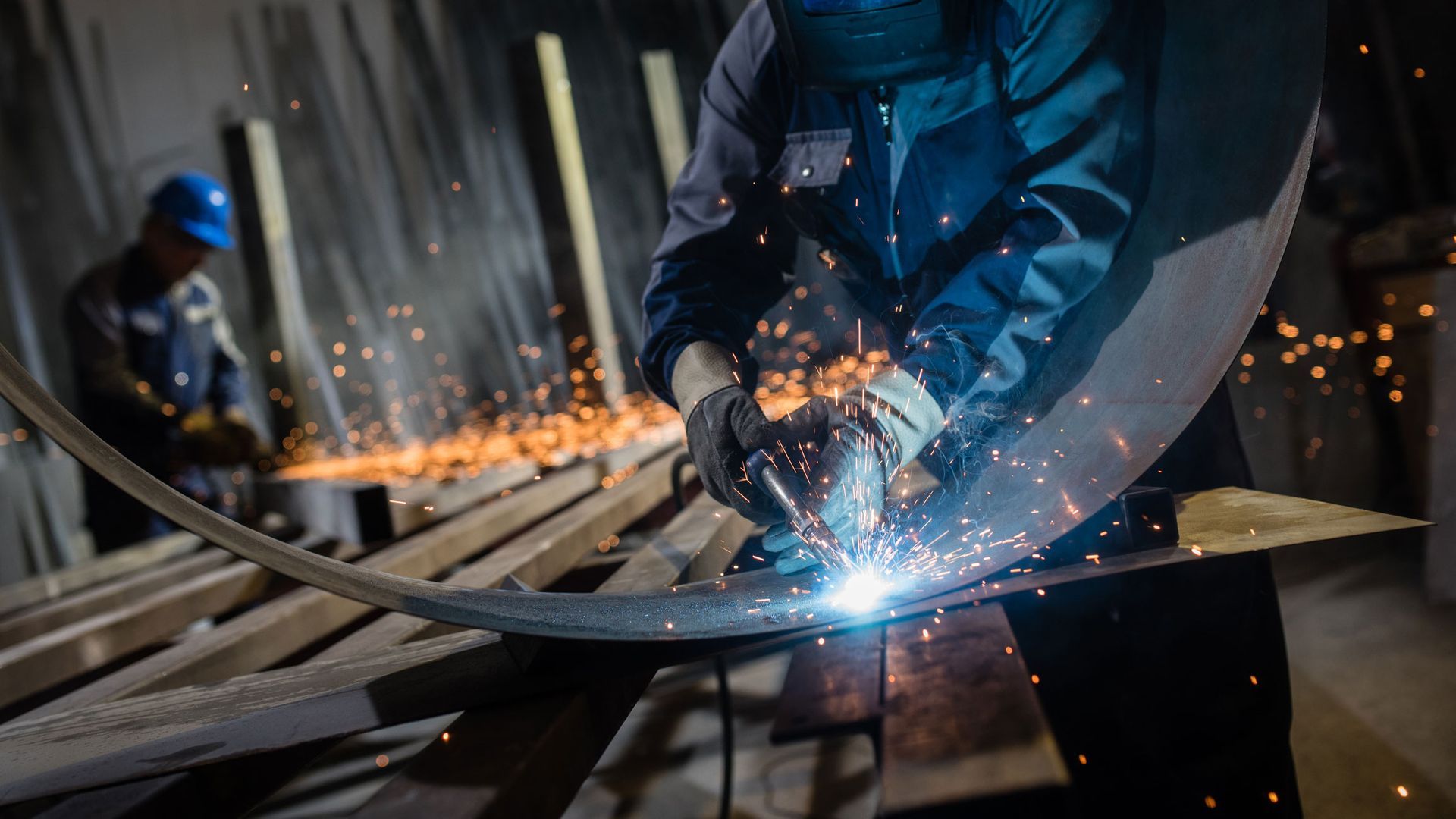 A man is welding a metal pipe in a factory.