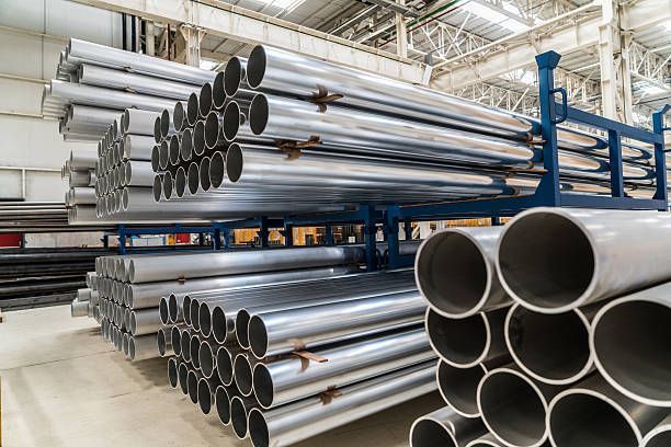 A bunch of metal pipes are stacked on top of each other in a warehouse.
