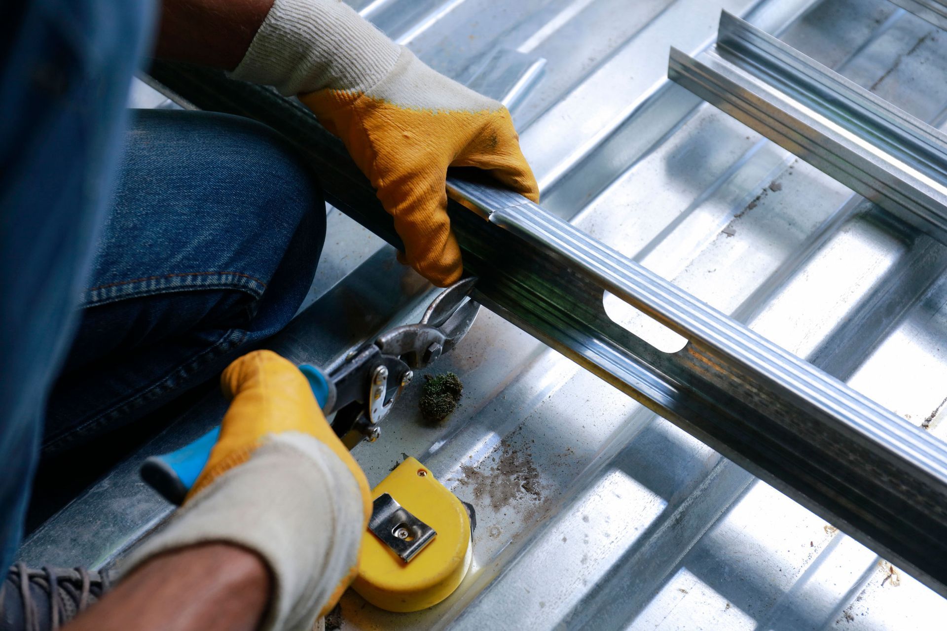 A man is working on a metal roof with a tape measure and pliers.