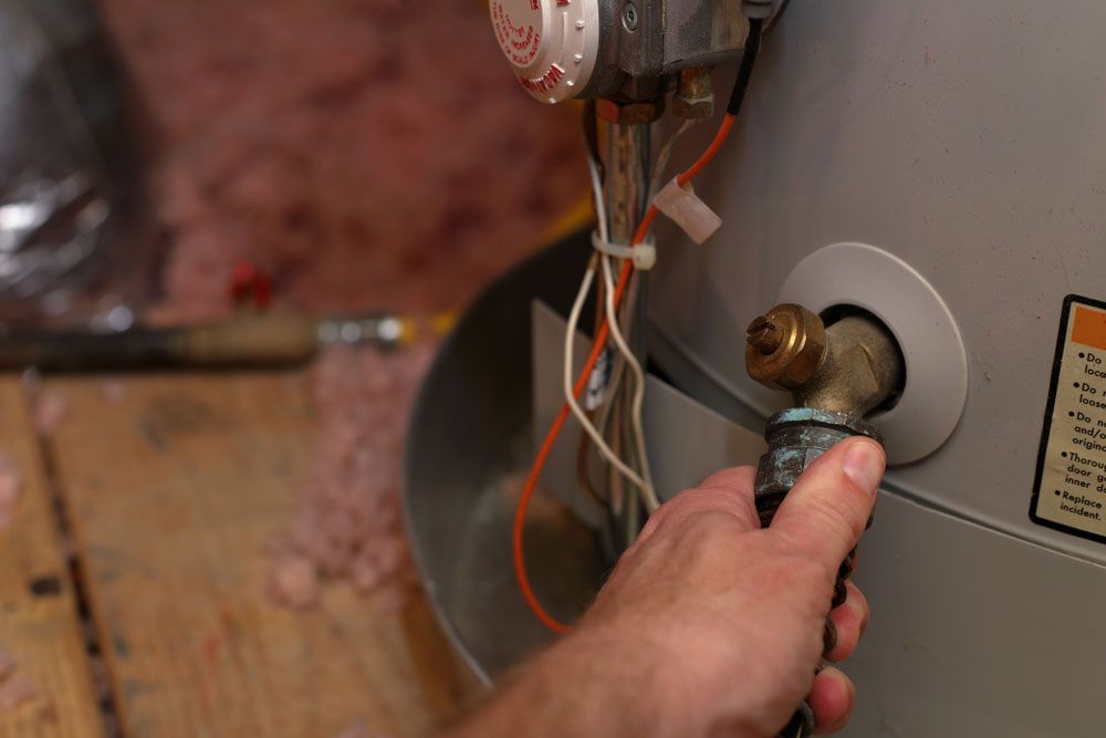 Hand attaches hose to water heater drain — Plumbers in Illawarra, NSW