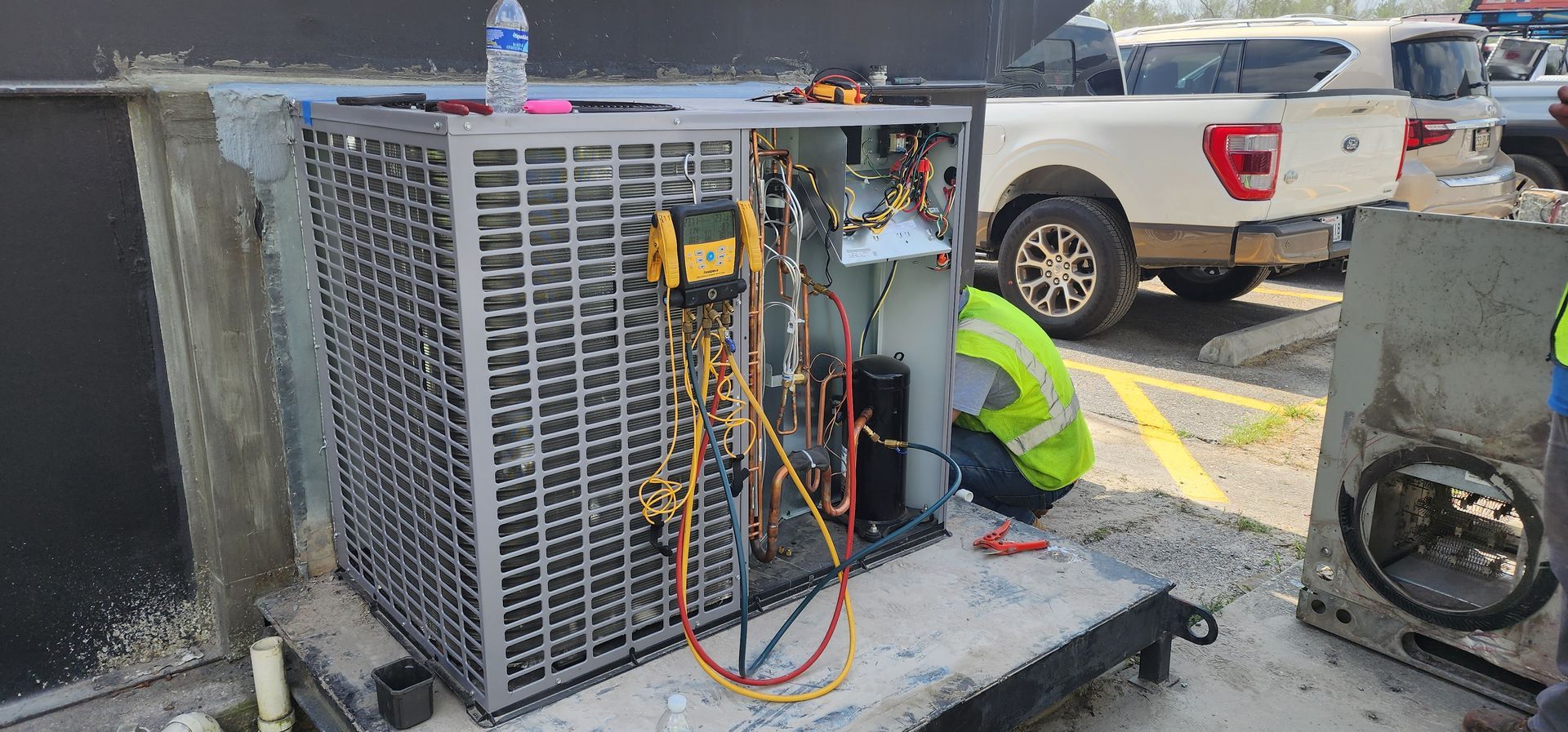 Person working on an air conditioning unit on a rooftop, with a water bottle and a white truck in the background.