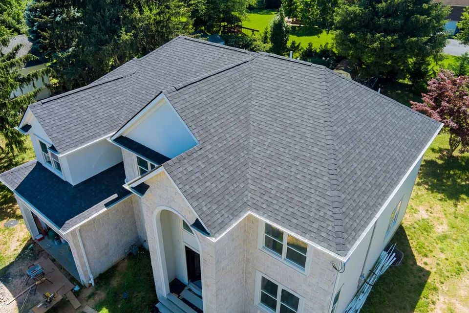 Aerial view of a light-colored house with a gray roof surrounded by green trees.