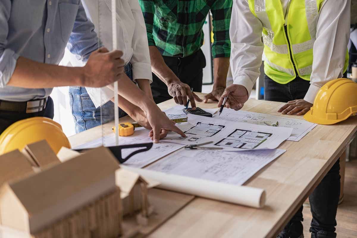 Construction team reviewing blueprints around a table with hard hats and a yellow safety vest