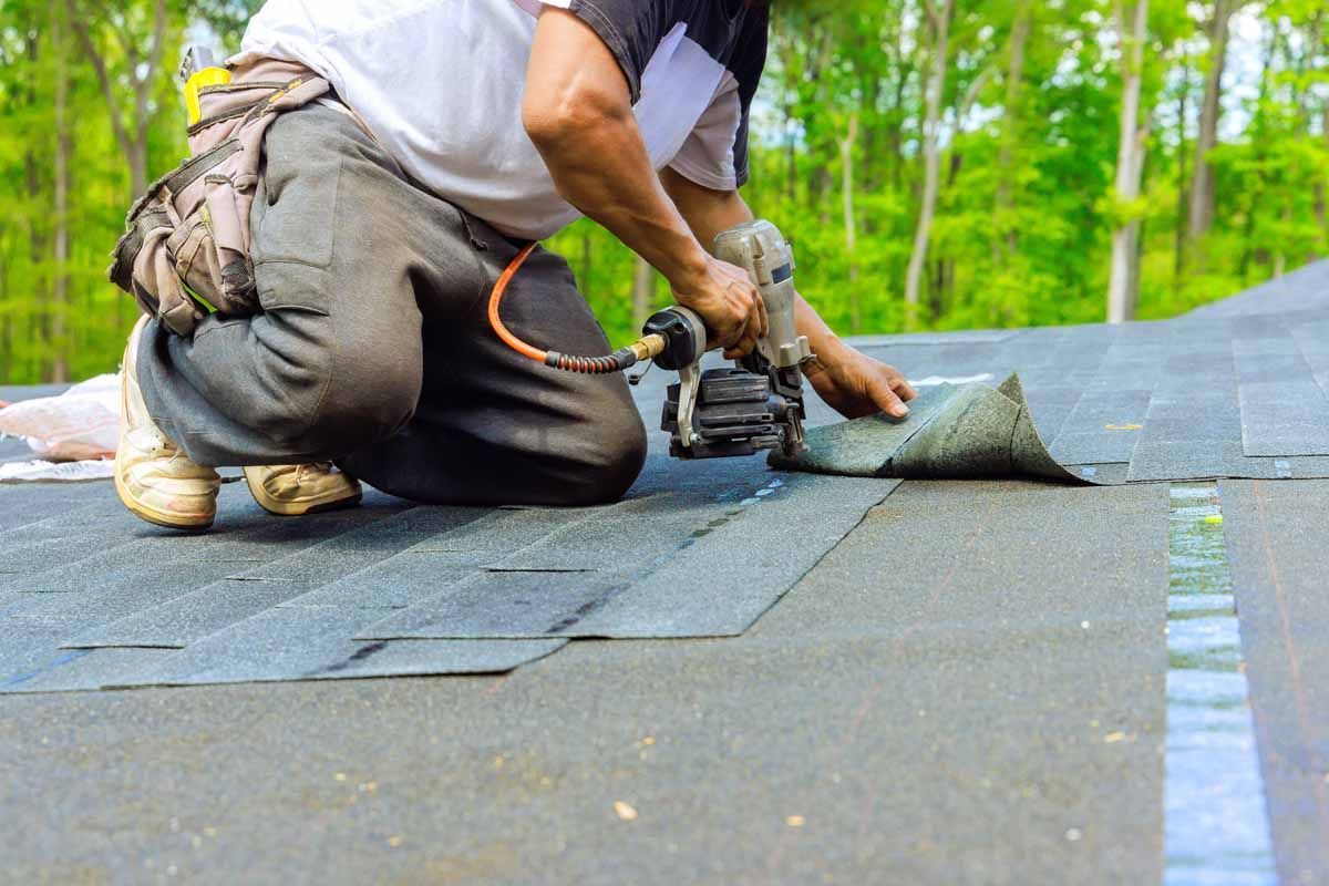 Worker installing shingles on a roof with a nail gun