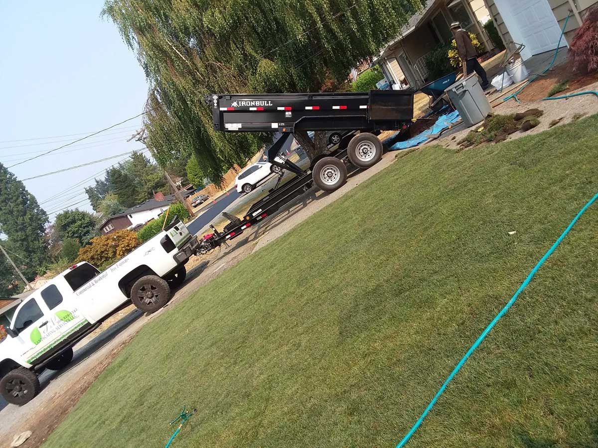 A dump truck is parked on the side of the road next to a white truck.
