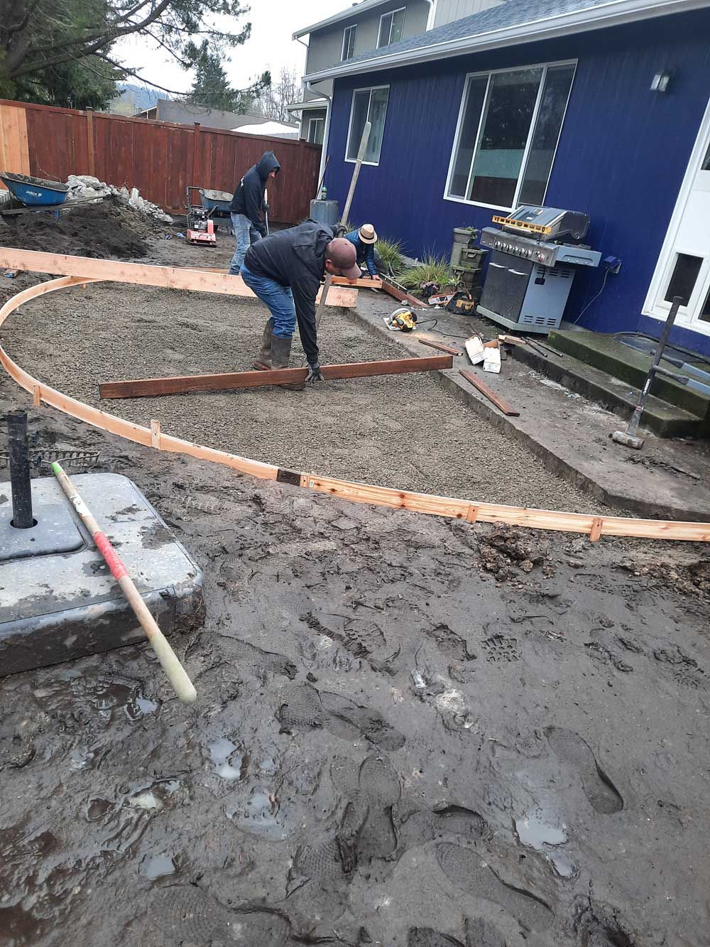 A group of men are working on a concrete patio in front of a blue house.