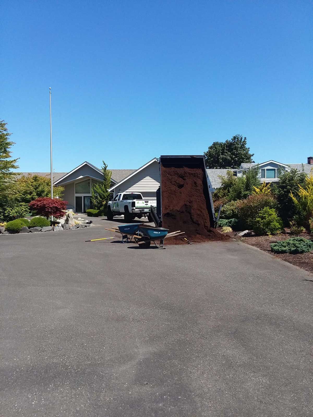 A dump truck is being loaded with dirt in front of a house