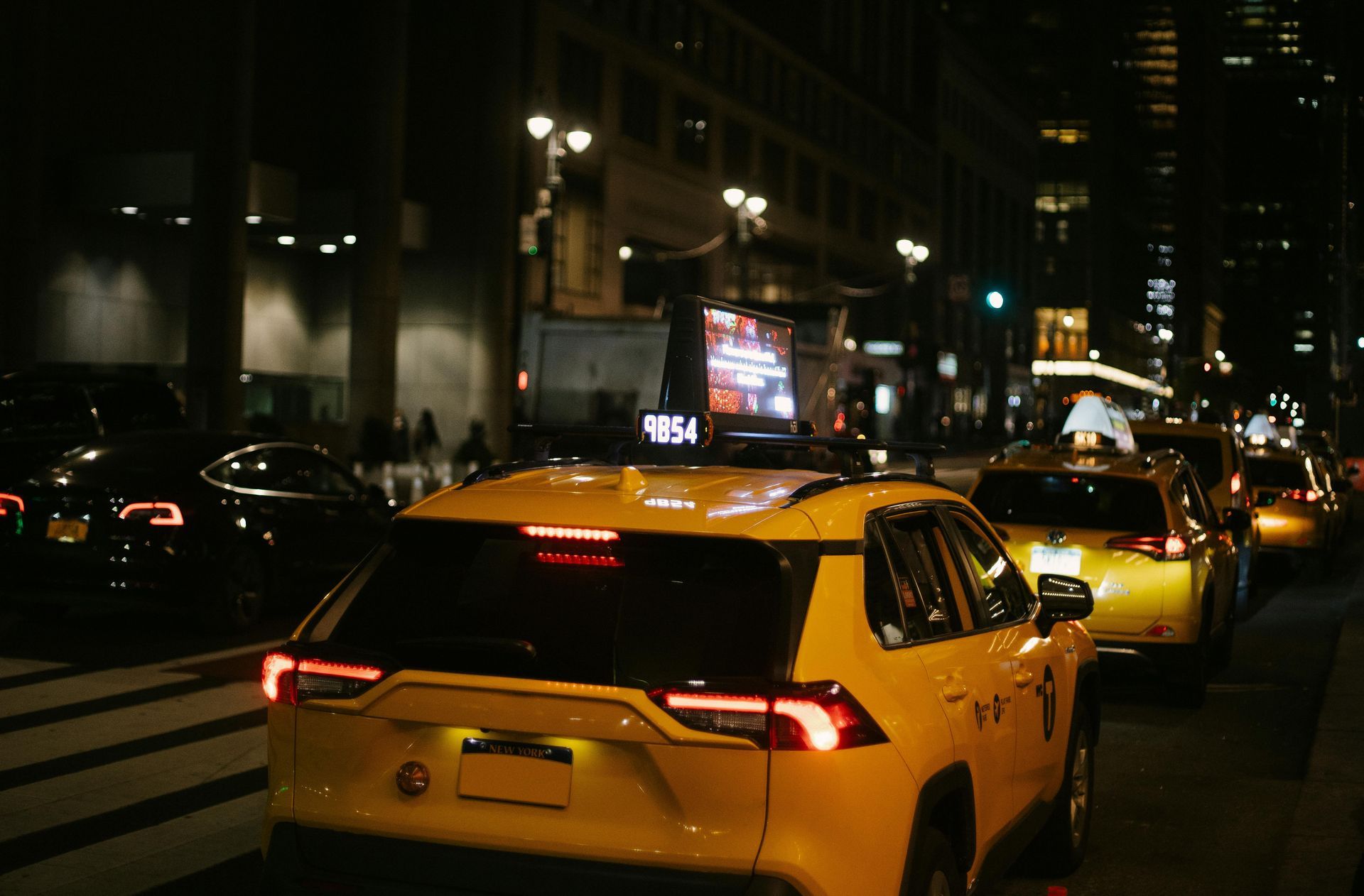 A row of yellow cars are driving down a street at night