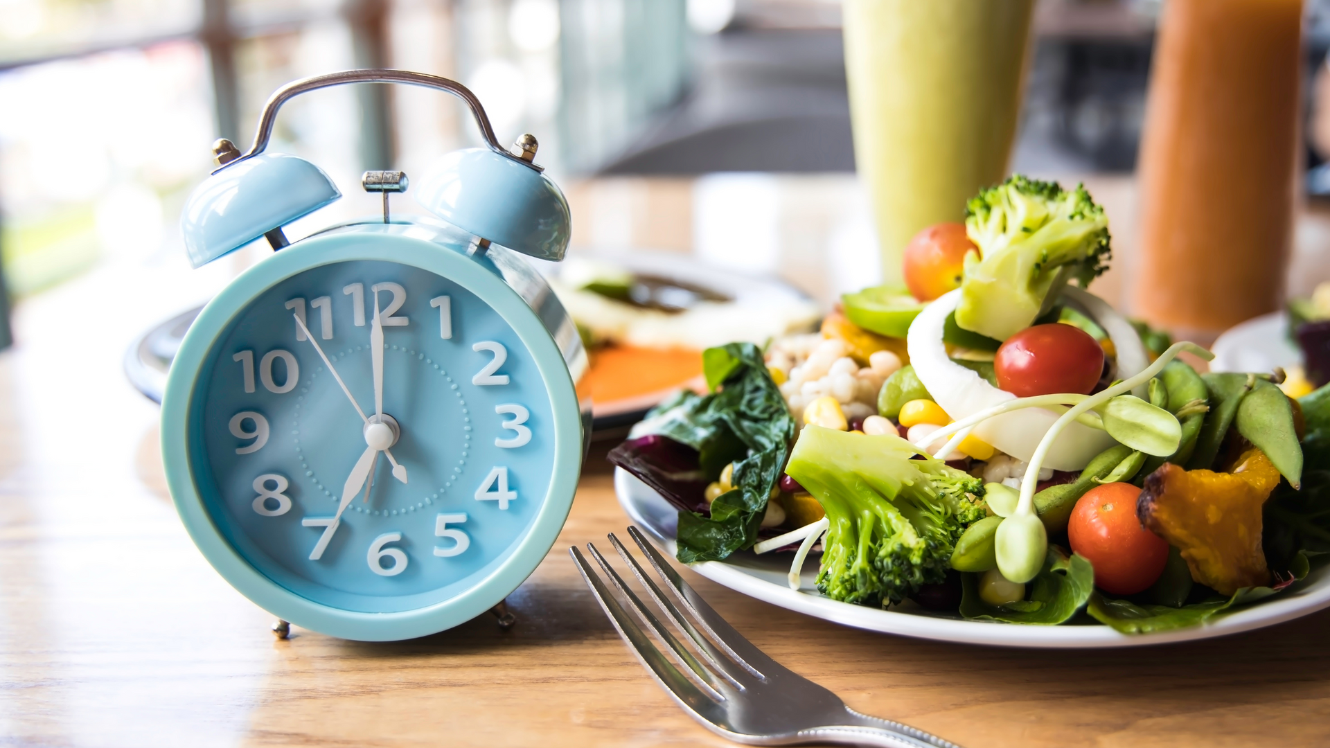 A baby blue clock on the left and a healthy salad on the right with smoothies in the background.