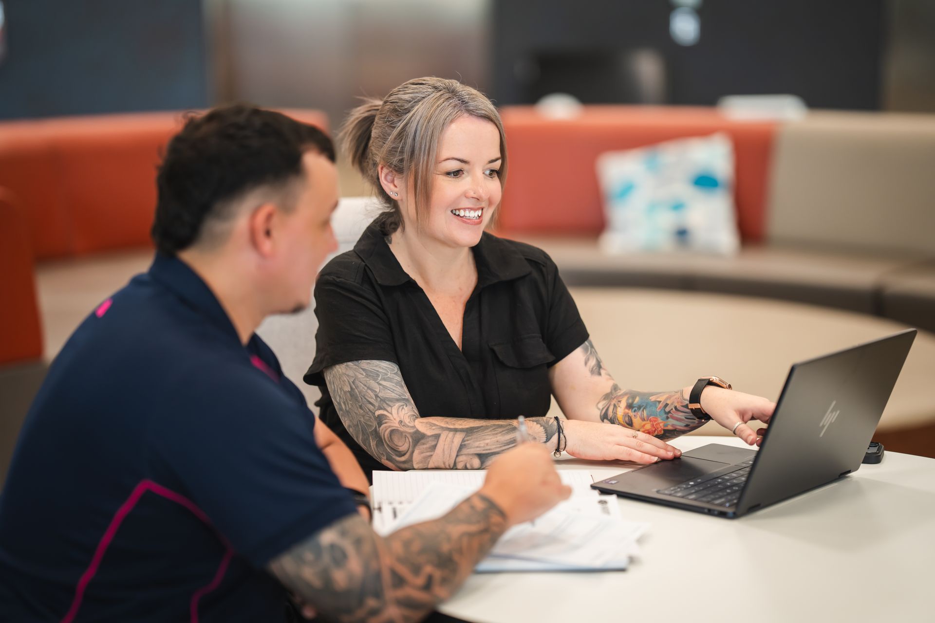Four businesspeople in suits talking in an office. One woman holds a pen and speaks.