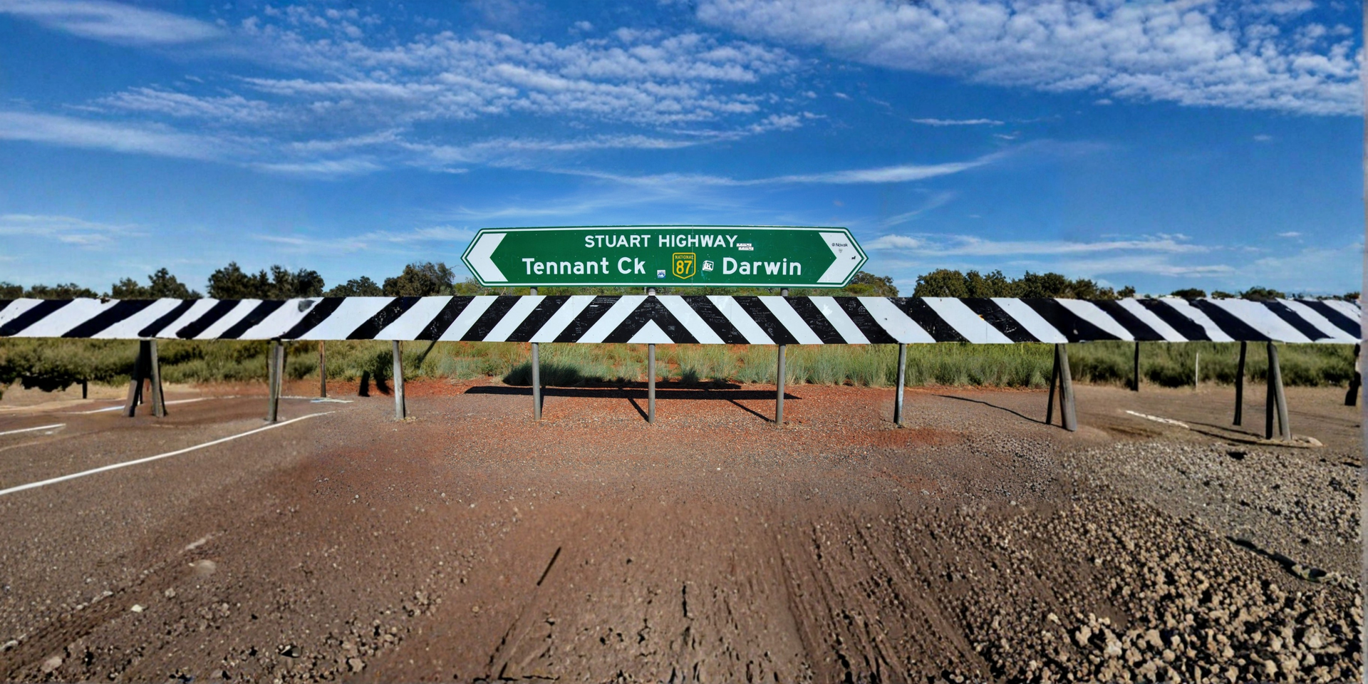 Three people smiling, interacting at a light-colored desk in an office. One in blue, two in black and burgundy.