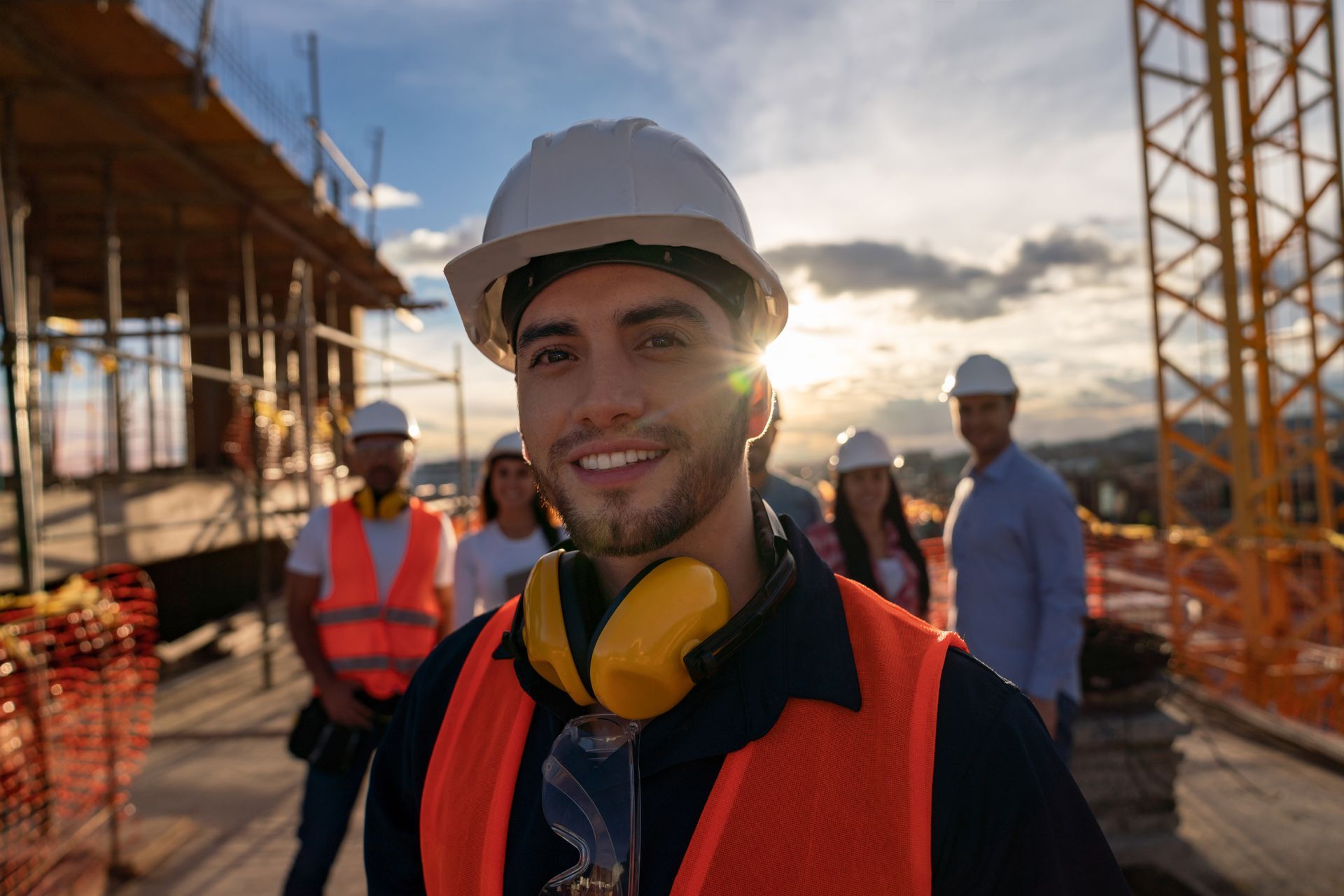 Construction worker on a roof hammering a nail, wearing safety gear and a hard hat.