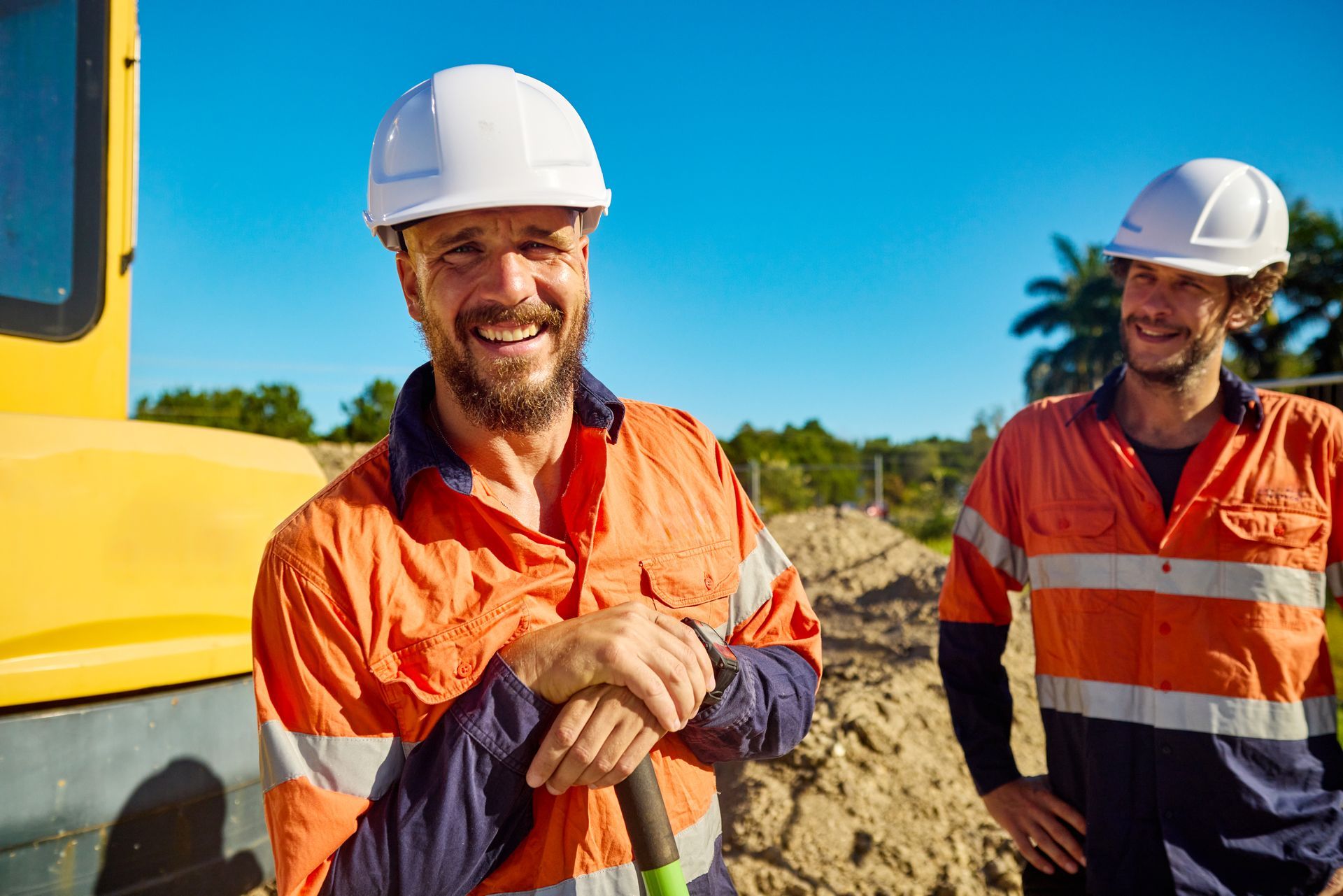 Two construction workers wearing hard hats, reviewing blueprints at a construction site.