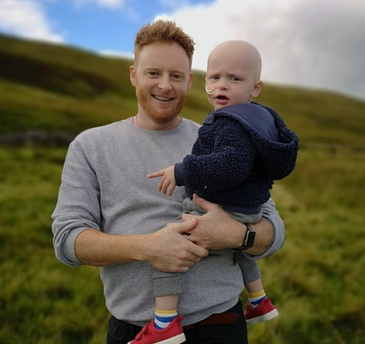 Website Sorted Three Peaks Challenge | A man is holding a baby in his arms in a field.