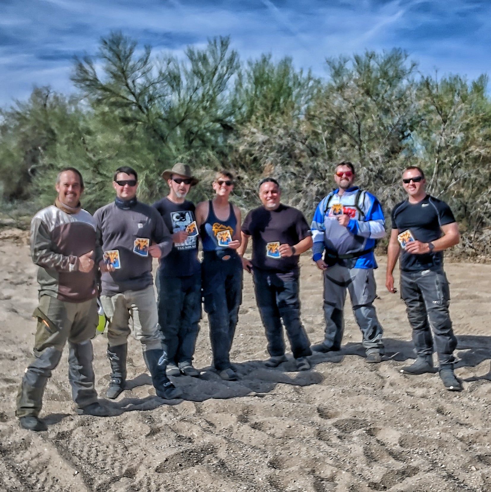 seven people standing in the desert and holding up Crooked Raven stickers